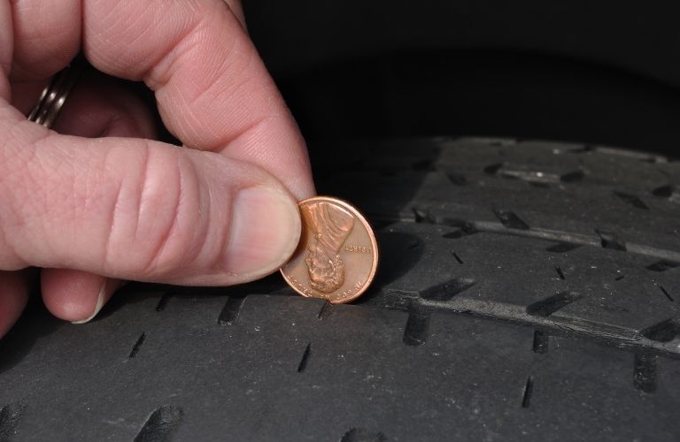 a hand checking the tread of a car using a coin