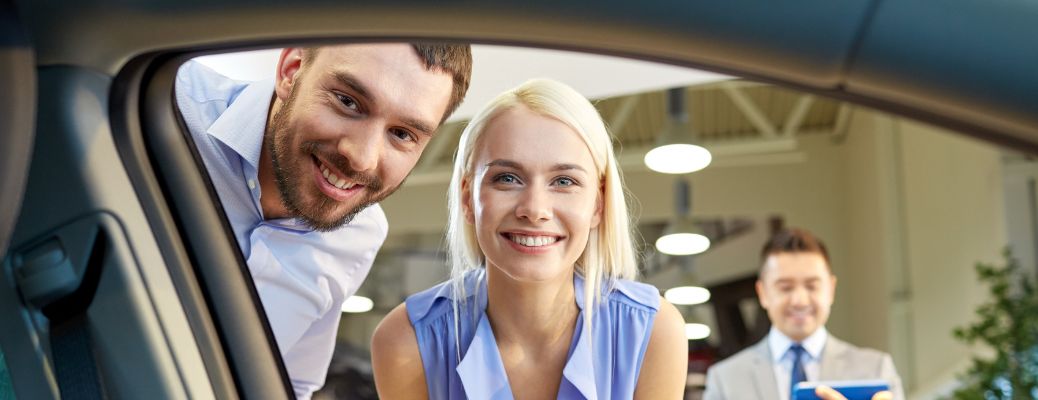 salesperson smiling in the background as a couple inspects a used car
