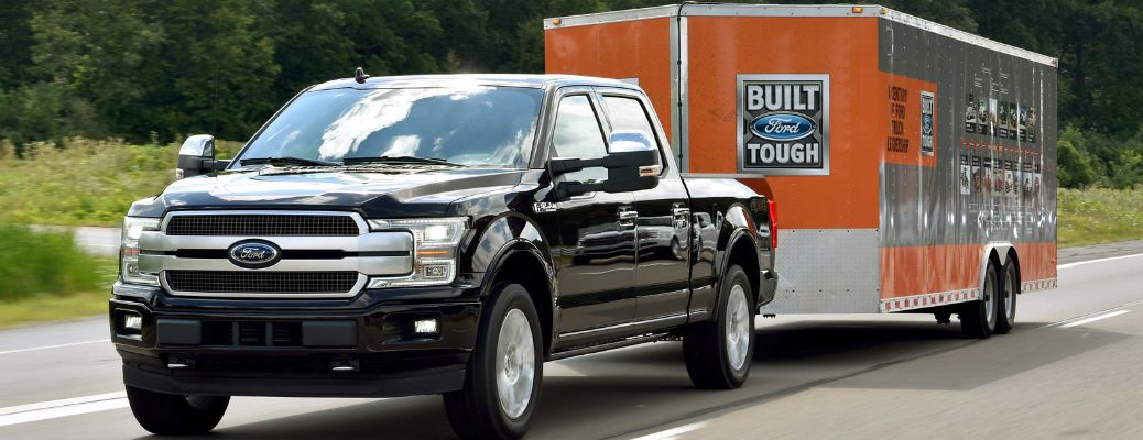 black 2018 ford f-150 towing orange ford trailer on highway