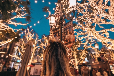 Woman Looking Up at Trees Covered in Christmas Lights
