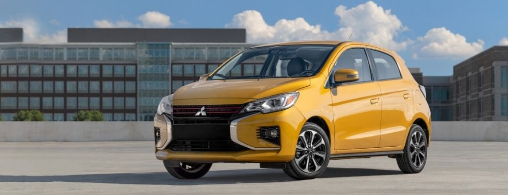 Front quarter view of a yellow 2022 Mitsubishi Mirage parked outside with glass buildings in the back