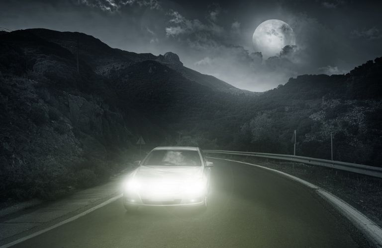 One car is running on the road at night under the fool moon sky.