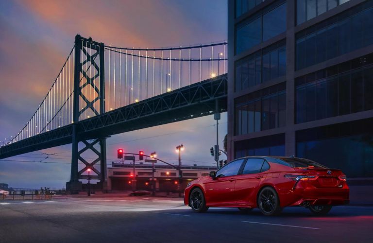 One red color 2023 Toyota Camry Hybrid is running on the road overlooking the bridge.