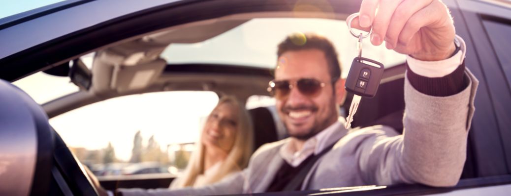 A smiling couple inside a car showing car keys