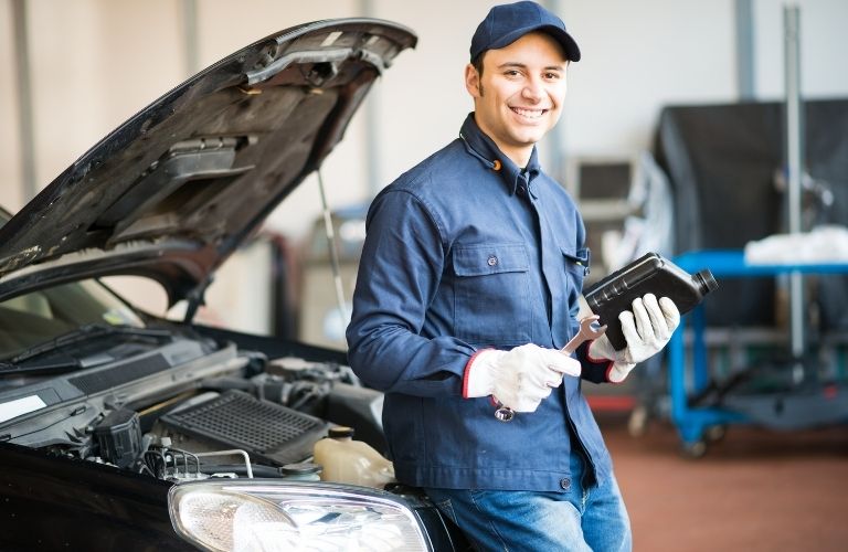 A smiling mechanic in front of a car