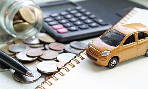 a small gold toy car set up next to a calculator, notebook, and jar of coins for calculating car financing