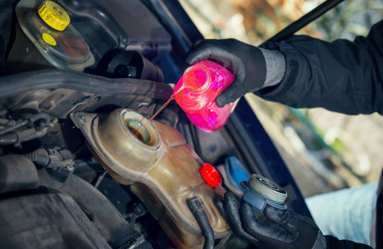 A mechanic's hand putting coolant in the engine